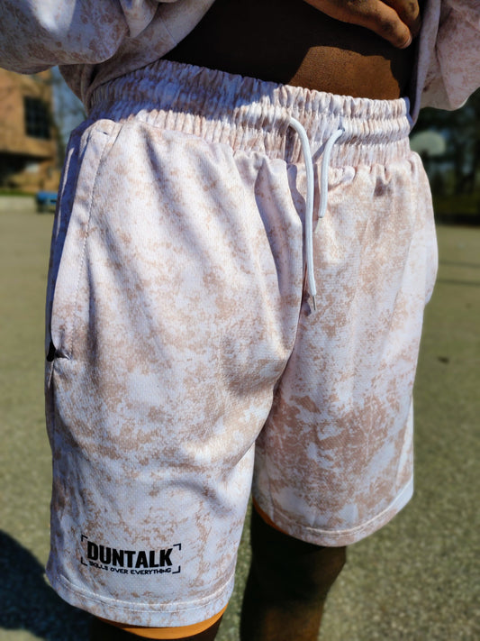 White basketball shorts with pink mud design, pockets, orange compression shorts underneath and tightening string at waist. Words on shorts say "Duntalk Skills Over Everything" in black font