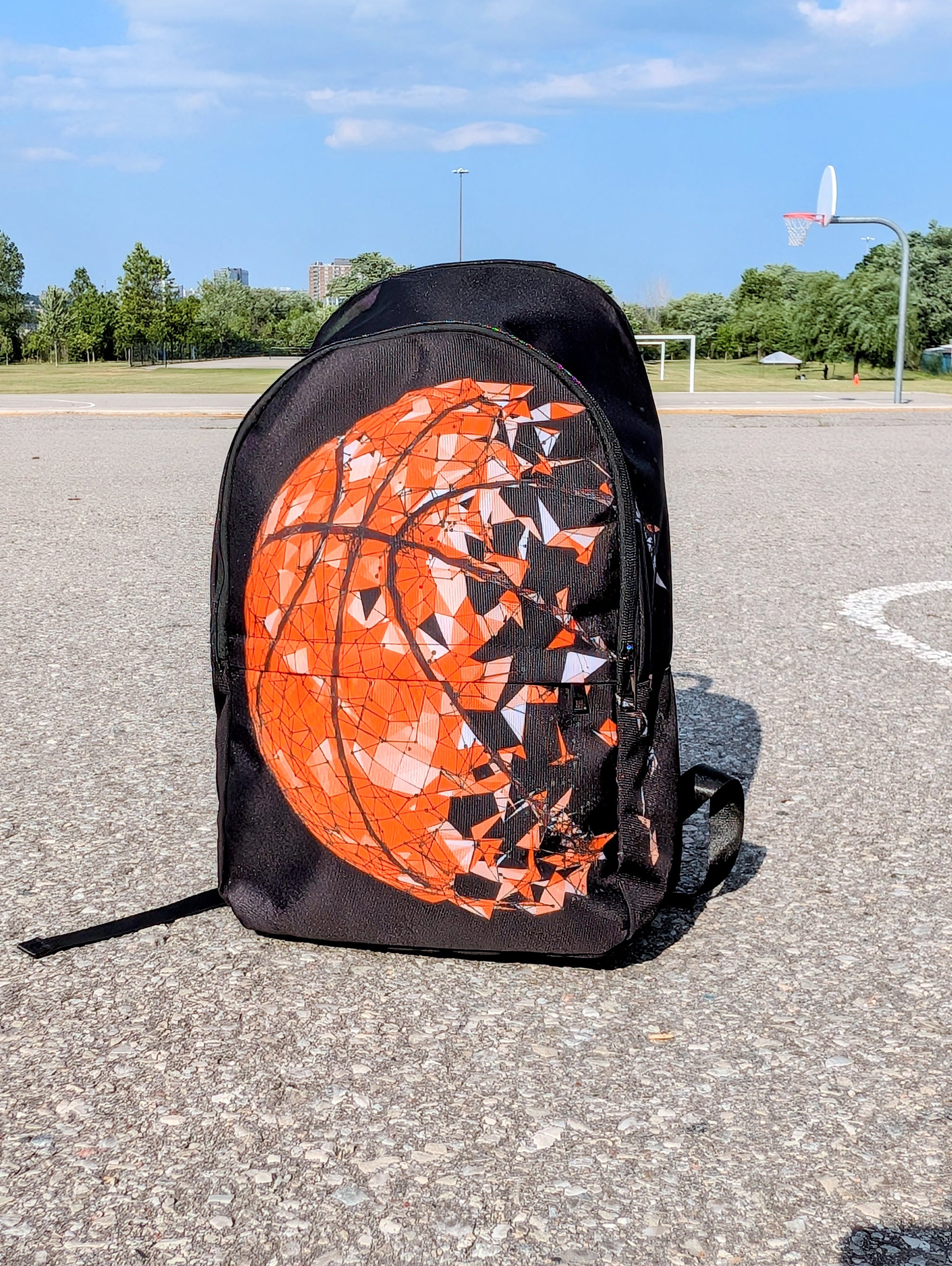 Front view of a backpack with basketball picture that breaks apart in pieces to the right on a basketball court.