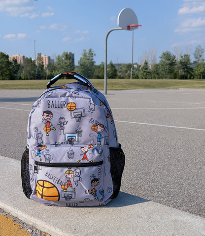 Backpack with cartoon drawn characters in action design on a concrete ledge near a basketball court.