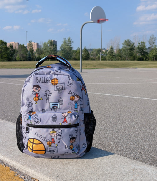 Backpack with cartoon drawn characters in action design on a concrete ledge near a basketball court.